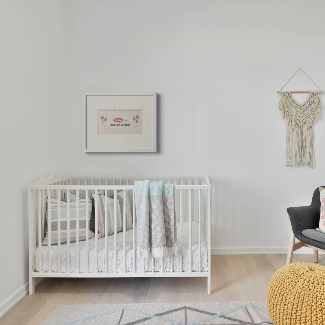 Quoteplume Kids frame above a white crib showing "June is one of a kind"